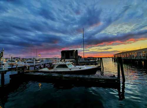 A serene marina at sunset, featuring a boat docked by the pier and colorful clouds reflecting in the water.