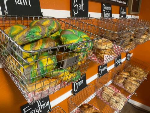 A display of colorful bagels in wire baskets, labeled with flavors like "Plain," "Salt," and "Everything."