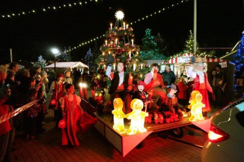 A festive parade scene with a decorated float, children in costumes, and glowing decorations amidst a crowd at night.