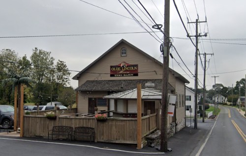 Exterior view of Olde Lincoln Tavern, featuring a wooden patio and surrounding power lines on a cloudy day.
