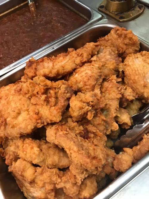 A tray of golden-brown fried chicken pieces, crispy and piled high, next to a container of brown sauce.