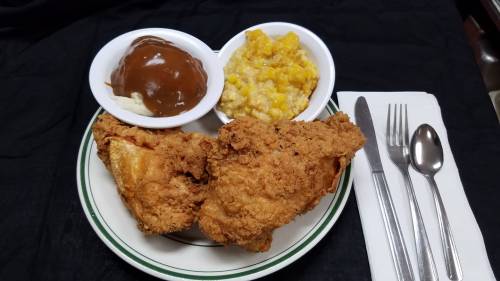 A plate of fried chicken with sides of mashed potatoes and corn pudding, accompanied by utensils on a napkin.