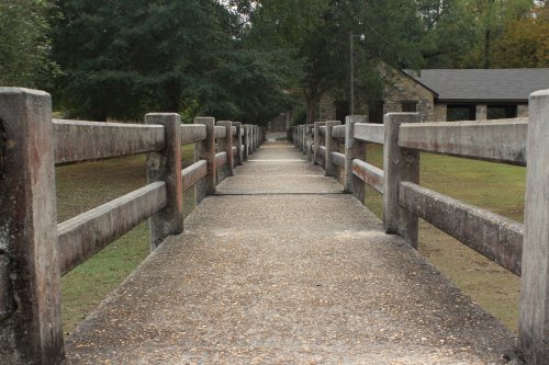 A long, narrow pathway with wooden railings, leading through a grassy area towards a building in the background.