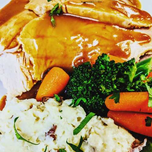 A plate of sliced turkey with gravy, mashed potatoes, steamed broccoli, and carrots, garnished with herbs.