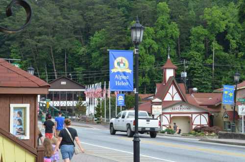 A street view of a small town with a sign for Alpine Helen, featuring shops, trees, and people walking.