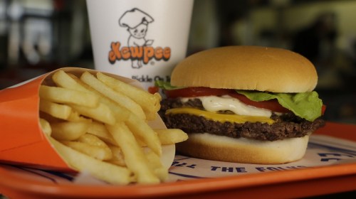 A cheeseburger with lettuce, tomato, and mayo, served with fries and a drink in a fast-food setting.