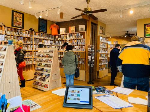 A cozy store filled with shelves of CDs and records, with customers browsing and a tablet on the counter.