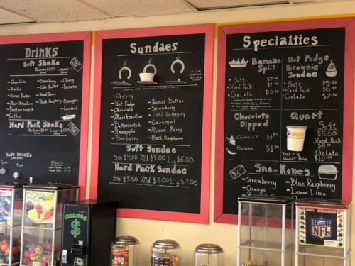 Chalkboard menu featuring drinks, sundaes, specialties, and prices in a colorful diner setting.