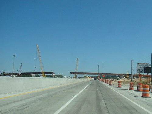 Construction zone on a highway with cranes and orange traffic barrels; speed limit sign reads 45 mph.