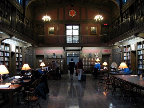 A spacious library with wooden furnishings, bookshelves, and people studying under warm lamps.