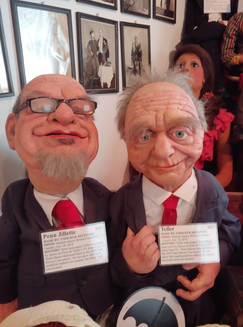 Two puppets resembling performers, dressed in suits, with name tags identifying them as Penn and Teller.