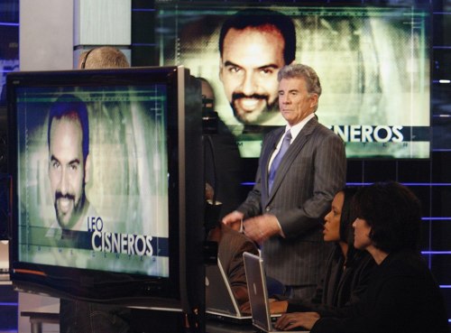 A news studio with a host and two guests, featuring a large screen displaying a man's image and name, Leo Cisneros.