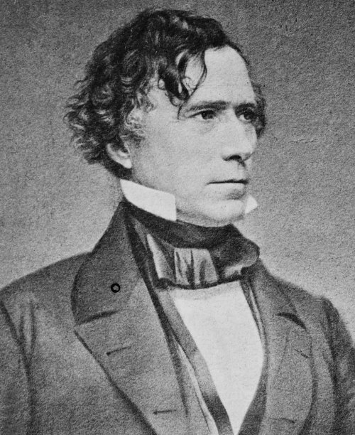 A historical portrait of a man with curly hair, wearing a formal suit and a high collar, looking to the side.