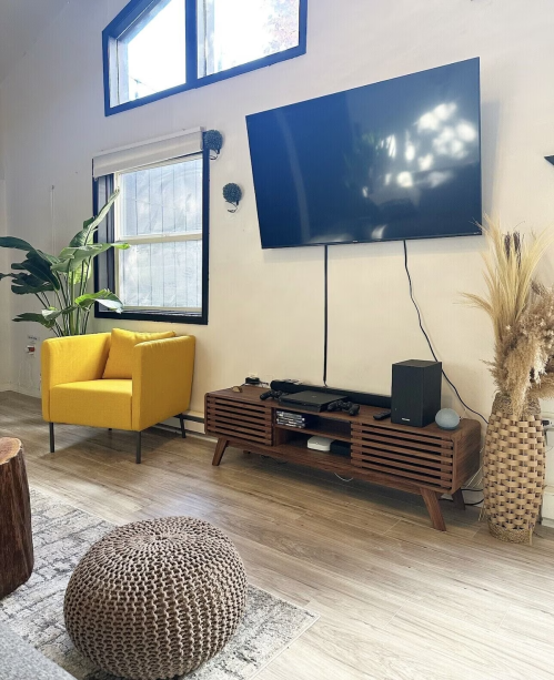 A cozy living room with a yellow chair, a TV on the wall, a wooden media console, and decorative plants.
