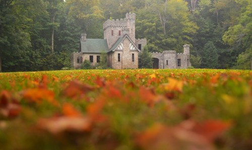 A stone castle surrounded by colorful autumn leaves and lush green trees in a serene forest setting.