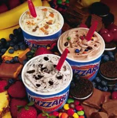 Three Dairy Queen Blizzard cups in various flavors, surrounded by colorful fruits and chocolate treats.