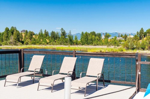 Lounge chairs on a deck overlooking a calm lake and green landscape with distant mountains under a clear blue sky.