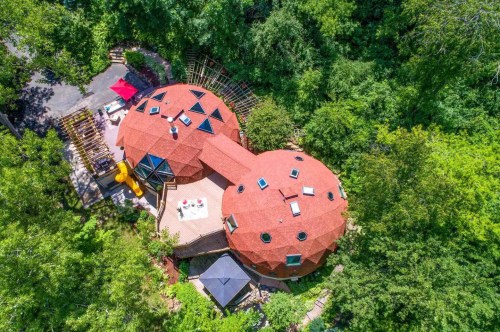 Aerial view of a unique, dome-shaped house surrounded by lush greenery and outdoor seating areas.