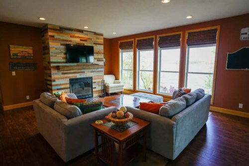Cozy living room with a fireplace, large windows, and comfortable seating, featuring warm colors and rustic decor.