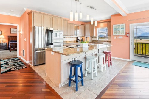 Bright kitchen with granite countertops, modern appliances, and colorful bar stools in a coastal-themed setting.