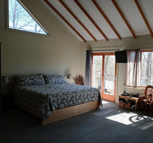 Spacious bedroom with a large bed, wooden beams, and glass doors leading to a balcony with natural light.