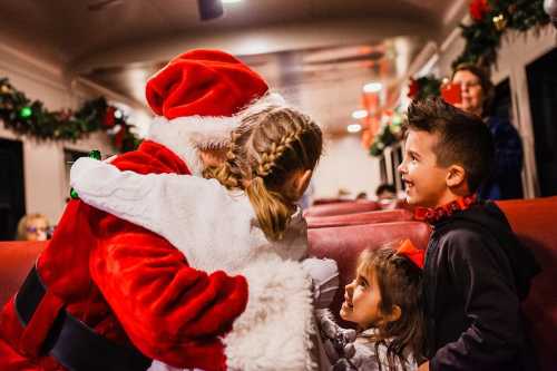 Children joyfully hug Santa Claus on a festive train, surrounded by holiday decorations and smiling faces.