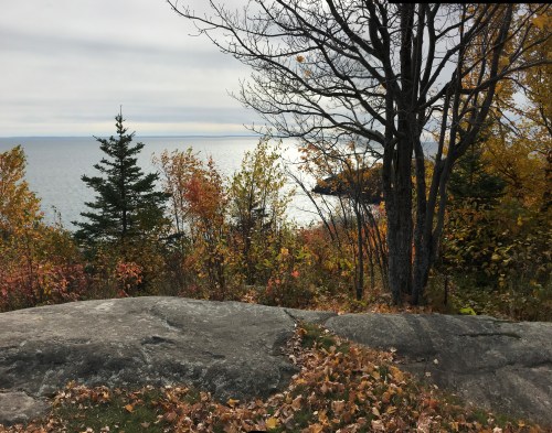 A rocky outcrop overlooks a lake surrounded by autumn foliage and trees under a cloudy sky.