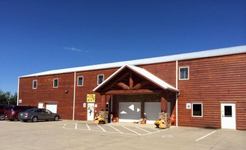 A large wooden building with a peaked roof, featuring a parking lot and decorative pumpkins in front. Clear blue sky above.