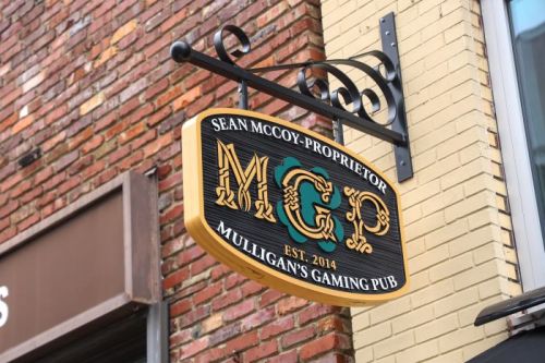 Sign for Mulligan's Gaming Pub, featuring "MGP" and "Sean McCoy - Proprietor, Est. 2014" against a brick background.