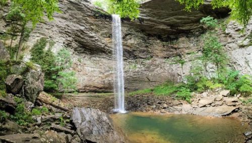 A serene waterfall cascades into a tranquil pool, surrounded by rocky cliffs and lush greenery.
