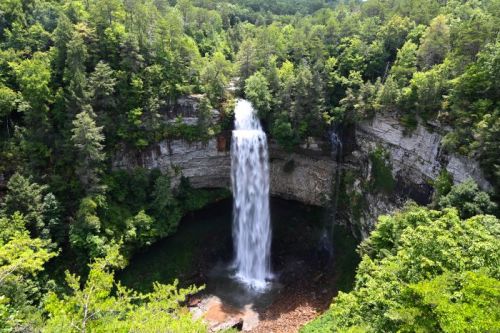 A stunning waterfall cascades down rocky cliffs, surrounded by lush green trees and foliage.