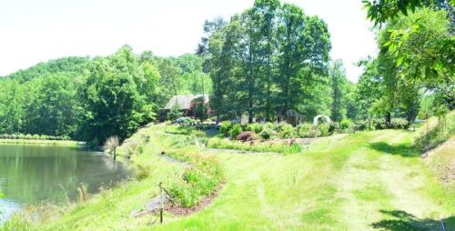 A serene landscape featuring a pond, lush greenery, and a house surrounded by trees and colorful flowers.