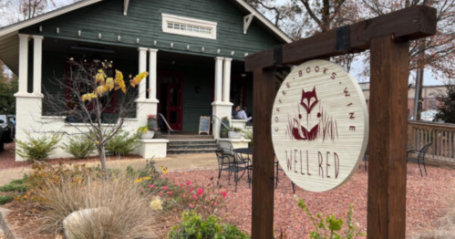 A cozy green building with a sign reading "Well Red" and outdoor seating, surrounded by plants and gravel.