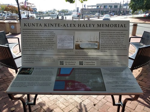 Sign at the Kunta Kinte-Alex Haley Memorial, detailing its significance and history, with a view of the waterfront.