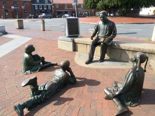 A bronze sculpture depicting a seated figure reading to four children on a brick plaza.