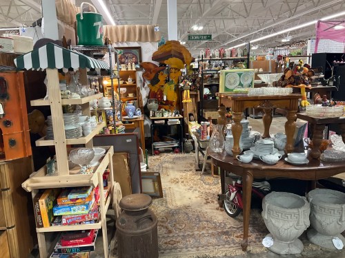A cozy antique shop filled with various vintage items, including furniture, dishes, and decor, arranged in a warm atmosphere.