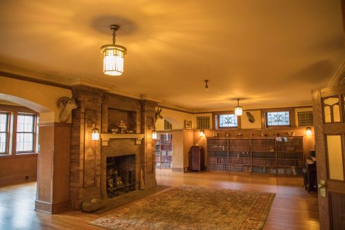 A spacious library with a fireplace, wooden shelves filled with books, and warm lighting.