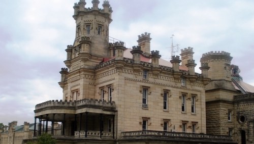 A grand, historic stone castle with turrets and a balcony, set against a cloudy sky.
