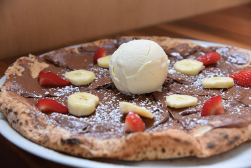A dessert pizza topped with chocolate spread, banana slices, strawberries, and a scoop of vanilla ice cream.