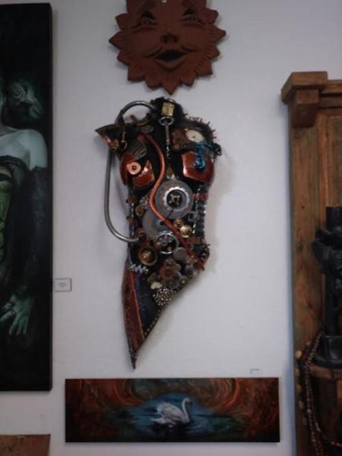 Artistic wall display featuring a torso sculpture made of metal gears and mixed media, alongside paintings.