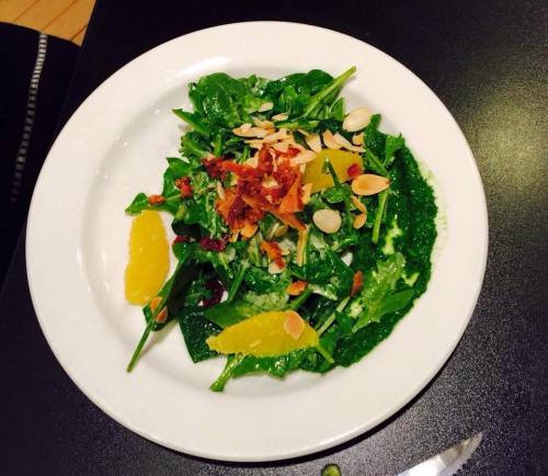 A fresh salad with spinach, orange segments, sliced almonds, and crispy bacon on a white plate.