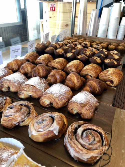 A display of various pastries, including croissants, muffins, and cinnamon rolls, dusted with powdered sugar.