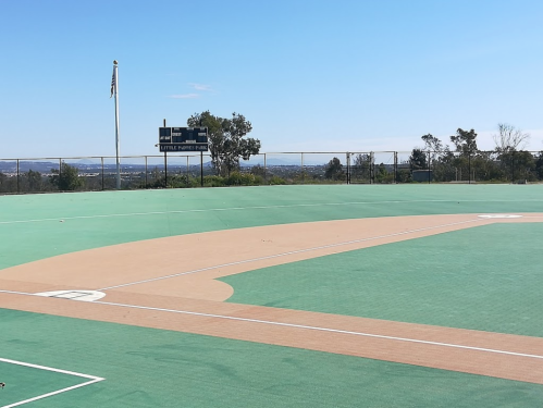 A baseball field with a scoreboard in the background, surrounded by trees and a clear blue sky.