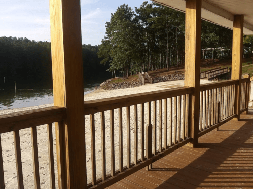 A wooden deck overlooking a sandy beach and calm water, surrounded by trees and a peaceful landscape.