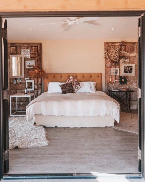Cozy bedroom with a large bed, decorative pillows, wooden accents, and a soft rug, viewed from an open doorway.