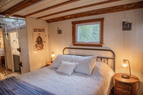 Cozy bedroom with a metal bed, blue bedding, wooden accents, and a window overlooking greenery.