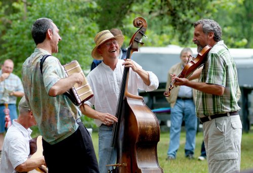 A group of musicians joyfully playing instruments outdoors, including a double bass, accordion, and violin.