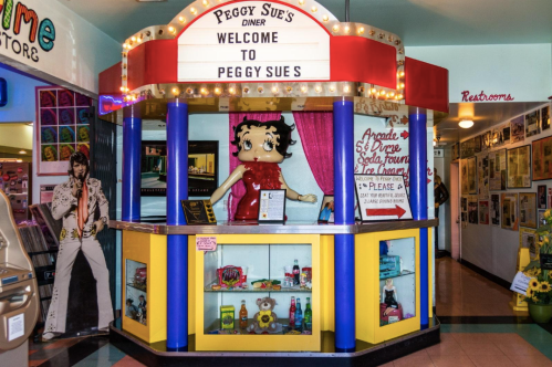 Colorful diner entrance with a Betty Boop figure, neon signs, and retro decor, welcoming visitors to Peggy Sue's Diner.