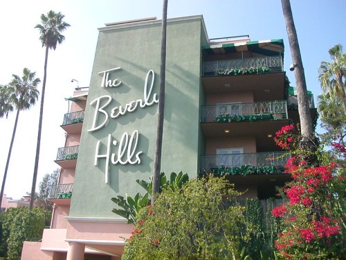 Exterior of The Beverly Hills hotel, featuring palm trees and vibrant flowers against a pastel green building.