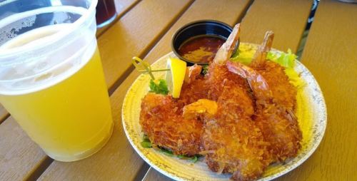 A plate of crispy fried shrimp with a lemon wedge and dipping sauce, alongside a glass of light beer.